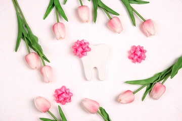 Festive dental background with tooth, bows and pink tulips on a white background with copy space for text.