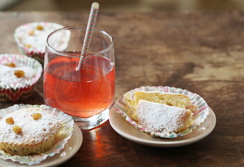 Small homemade cakes with powdered sugar, baked in paper tins with a glass of juice.
