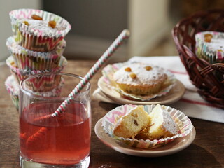 Small homemade cakes with powdered sugar, baked in paper tins with a glass of juice.