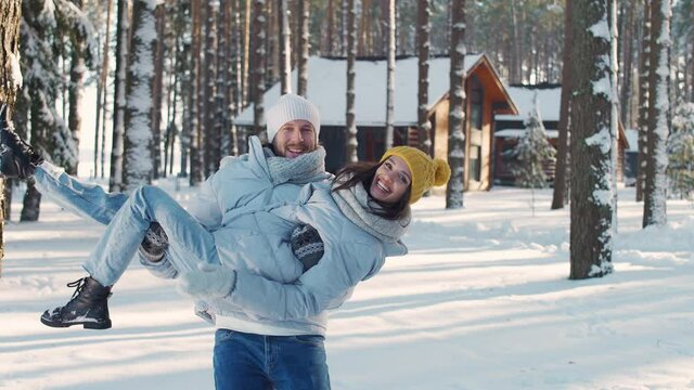Young cheerful couple in a winter forest, man and female take a photo on camera against the background of a winter forest, sunny winter weather, man holds a girl in his arms.