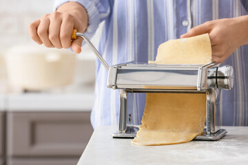Woman making pasta with machine at table in kitchen
