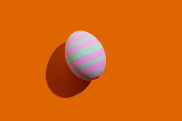 Easter egg. Festive decoration. Holiday gift card. Abstract background. Pink painted paschal symbol with light green stripes pattern isolated on orange copy space.