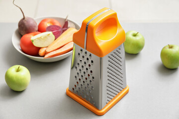 Metal grater, apples and vegetables on kitchen table