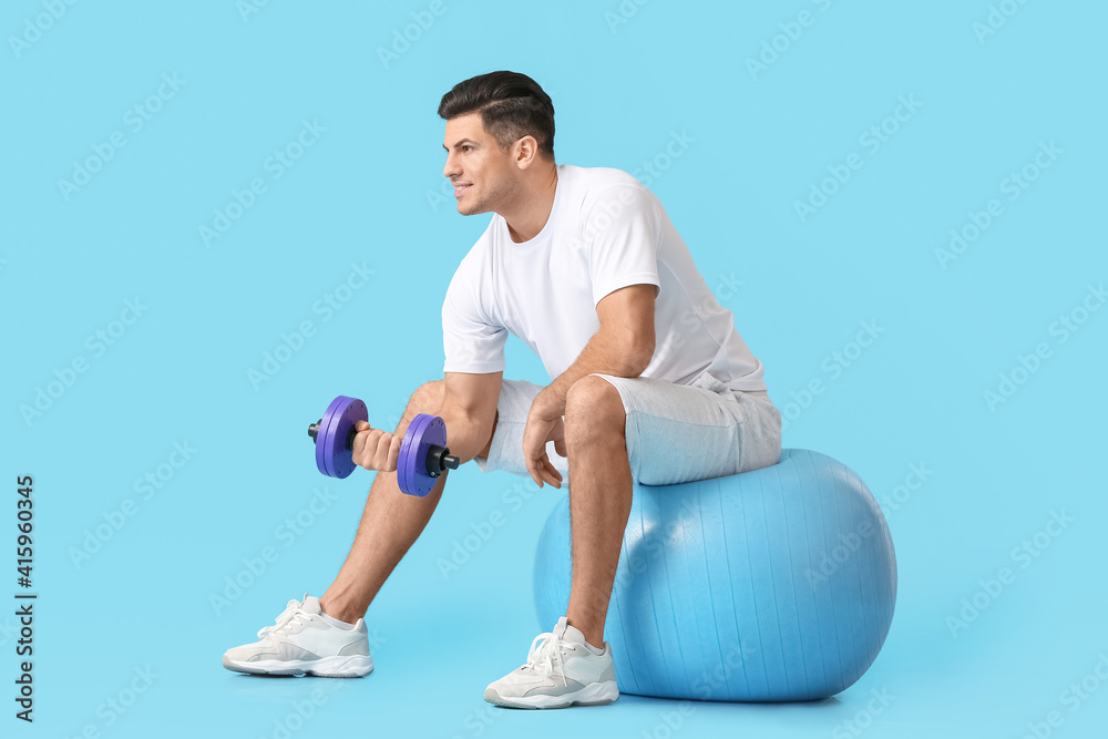 Wall mural sporty young man training with dumbbell on color background