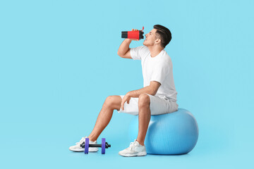 Sporty young man drinking water on color background