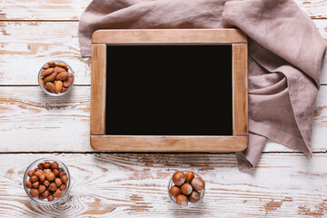 Empty chalkboard with healthy nuts on white wooden background