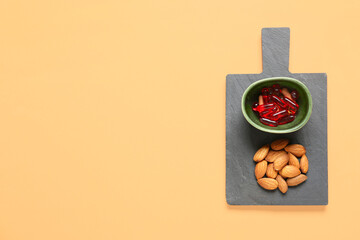 Bowl with pills and almond nuts on color background