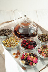 several varieties of herbal and berry tea and a kettle with hot fresh tea on a wooden tray and beige linen tablecloth. Vertical photo. Place for text.