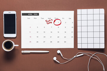 Calendar with marked date of April Fool's Day, mobile phone and stationery on color background