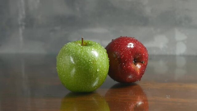 Two fresh apples, green and red in drops of water, lie on a wooden brown table. Dolly fruit shooting. Close-up. Natural food concept
