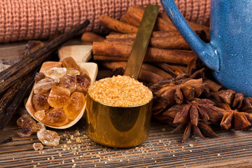 Cinnamon sticks, star anise, vanilla beans and different brown sugar with stack of knits on a wooden background. Top view. Sweet spices concept.