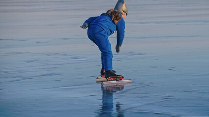 The child train on ice professional speed skating. The girl skates in the winter in sportswear, sport glasses, suit. Children speed skating short long track, kid sport. Outdoor slow motion.