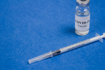 Vial of Covid-19 vaccine and syringe for injection on a blue background.