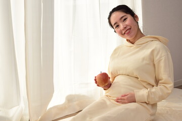 A pregnant woman in her twenties has an apple in front of her big belly. A healthy diet is important during pregnancy. 