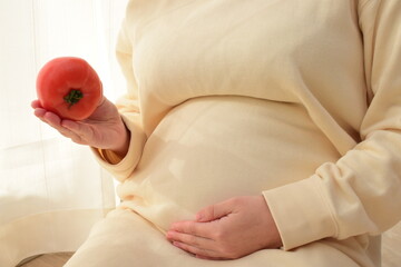A pregnant woman in her twenties has a tomato in front of her big belly. A healthy diet is important during pregnancy. 