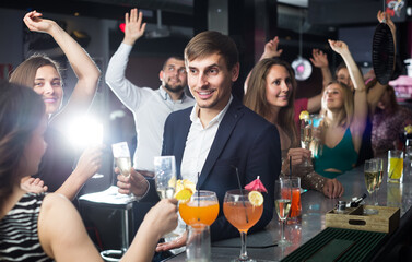 Men and women are dancing in a restaurant with cocktails in their hands