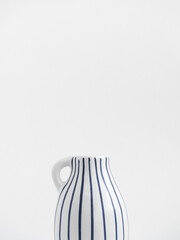 White ceramic jug with blue stripes isolated on white background. Trend minimalistic composition. Boho or Scandinavian style poster in modern home interior. Copy space. Close-up