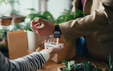 Customer with smartwatch paying in plant store, contactless payment concept.