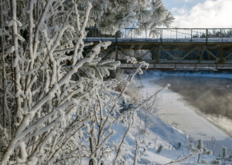 winter landscape, fog on the river, bridge silhouette in the background, beautiful white frost covering trees and grass on the river bank