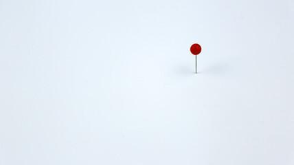 A small red pin with white background. Minimalist concept for objective, target, point and mark. Selective focus.