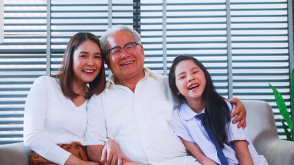 Happy family with grandfather, mother and little daughter spending time together in living room.