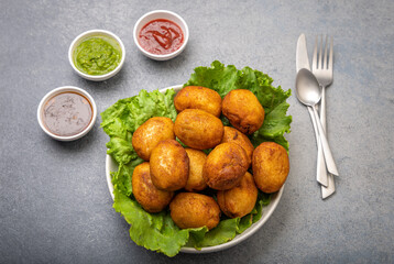 bread rolls stuffed with potatoes placed on a lettuce leaf served with green and red sauces
