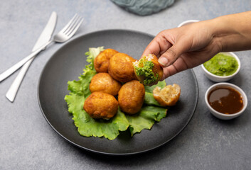 A girl is taking a bite of bread rolls stuffed with potatoes served with green and red sauces
