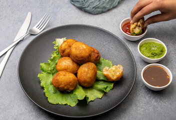 A girl is taking a bite of bread rolls stuffed with potatoes served with green and red sauces