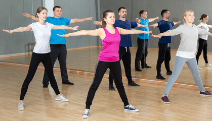 Sporty females and males doing stretching workout during group training at dance class