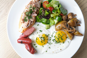 breakfast of fried eggs, sausages, vegetables and potatoes on a white plate, top view