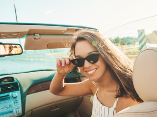 Portrait of young beautiful and smiling hipster female in convertible car. Sexy carefree woman...