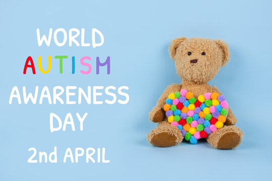 World Autism Awareness Day concept - sad teddy bear with multicolored heart sitting against blue background. Autism spectrum disorder and child mental health concept, selective focus