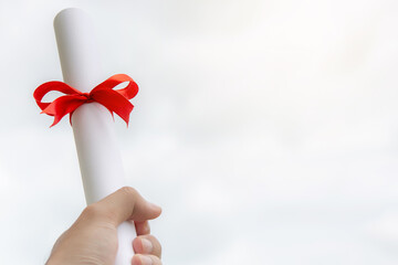 Hand holding a graduation certificate with a red ribbon Raise to the sky