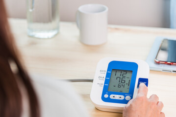Woman checking her blood pressure with automatic blood pressure monitor at home, health and medicine home healthcare concept.