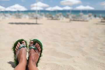Feet in beach slates of green grass on a sandy beach with sun umbrellas