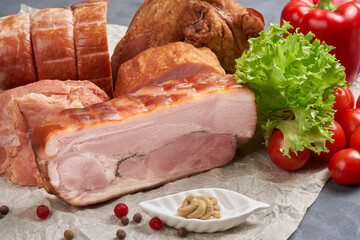 Close-up of assorted pieces of smoked pork with mustard on parchment. Still life with semi-finished meat.