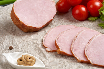 Close-up of traditional sliced smoked pork tenderloin on paper with fresh tomatoes and mustard. Classic meat products, delicacies. Still life of food