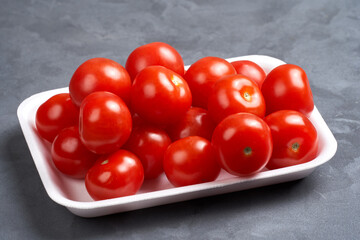 Lots of red cherry tomatoes on a substrate. Gray background, side view, close-up