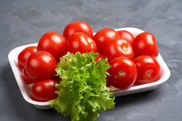 Heap of cherry tomato with lettuce on a substrate. Gray background, side view, close-up