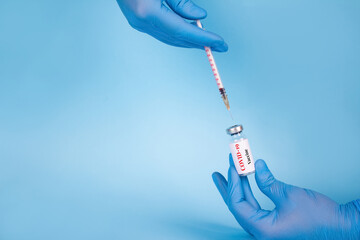 Doctor injecting vial dose of COVID-19 vaccine with syringe against blue background with copy space...