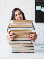 Young teacher sitting with pile of books looking away ready for lesson