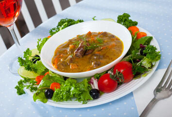 Appetizing goulash with chicken hearts served in white bowl with greens and lime