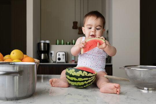 Cute baby sitting on kitchen counter holding watermelon slice
