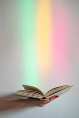 Opened book. Available knowledge. Enjoy study. Erudition new information. Female hand with story tome on blur rainbow overlay glowing neon lights background.