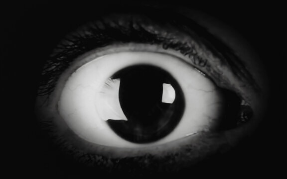 The scared big eye of a woman, looking at the camera. Detail macro shot. Film-noir style.
