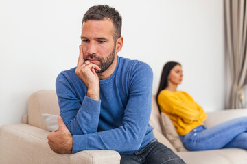 Fototapeta premium Young couple sitting on sofa being angry after fight. Couple Having Argument At Home. Girlfriend and boyfriend sitting next to each other angry, couple fighting