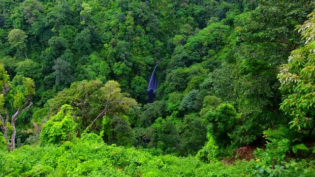 Aerial view of man standing at a viewpoint, flying a drone towards the Tiu Kelep waterfall, in Lombok