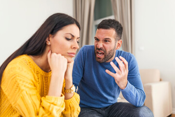 Obraz premium Young sad afraid woman and her violent screaming man. Young couple fighting at home, boyfriend shouting at girlfriend. Stressed out couple having problems. Divorce concept.