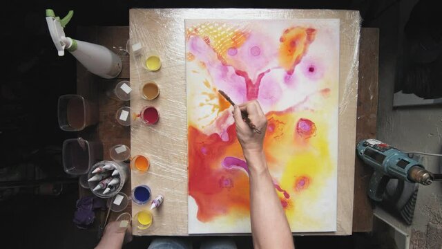 Fluid Art. Abstract colorful painting. Top view of male artist uses paintbrush to paints an abstract shapes on wet canvas