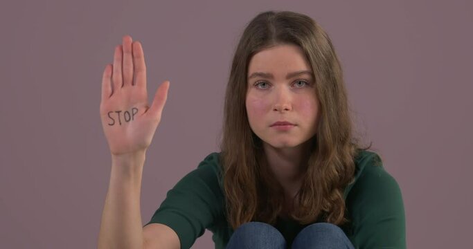 Close-up portrait of Caucasian woman sitting on the floor and raising hand with stop inscription on palm. Stop violence against women. Female rights. Abuse issue